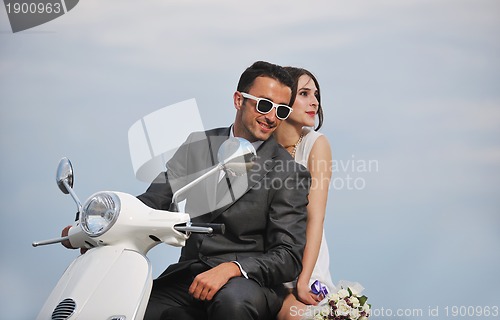 Image of just married couple on the beach ride white scooter