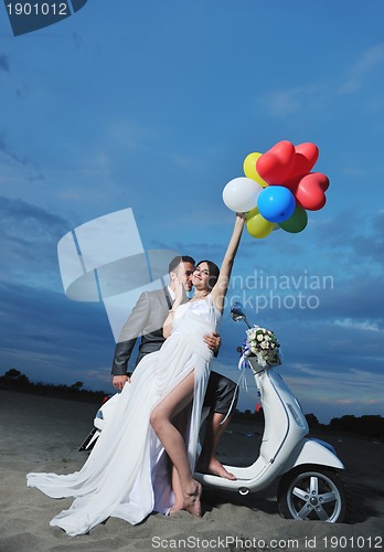 Image of just married couple on the beach ride white scooter