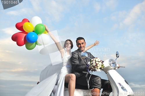 Image of just married couple on the beach ride white scooter