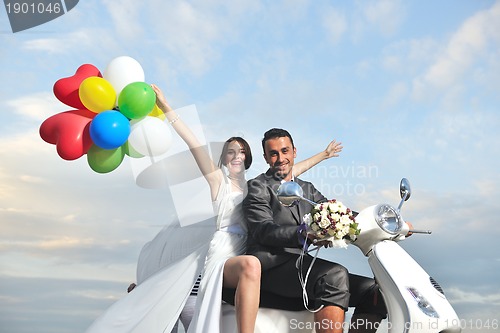 Image of just married couple on the beach ride white scooter