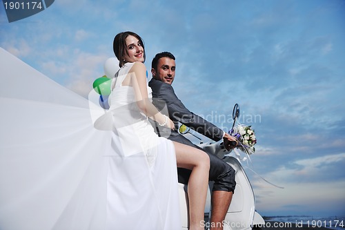 Image of just married couple on the beach ride white scooter