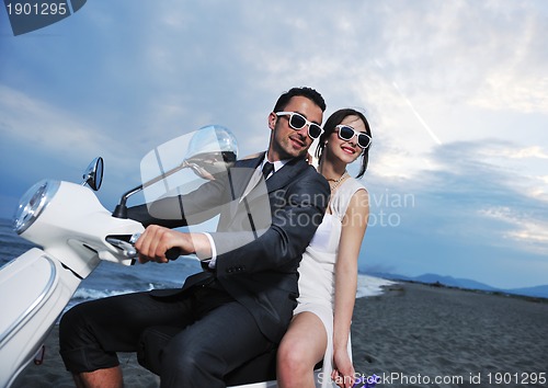 Image of just married couple on the beach ride white scooter