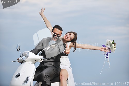 Image of just married couple on the beach ride white scooter