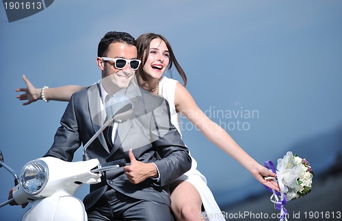 Image of just married couple on the beach ride white scooter