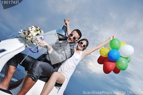 Image of just married couple on the beach ride white scooter