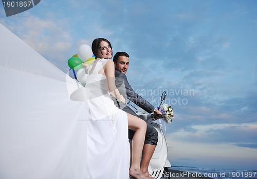 Image of just married couple on the beach ride white scooter