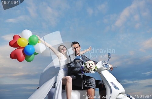 Image of just married couple on the beach ride white scooter