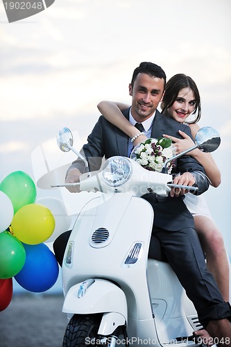 Image of just married couple on the beach ride white scooter