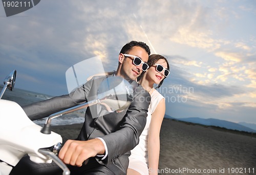 Image of just married couple on the beach ride white scooter