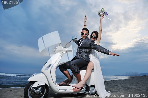 Image of just married couple on the beach ride white scooter