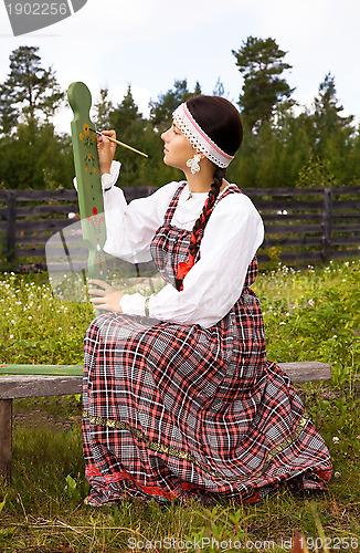 Image of Girl in national costume paints a spinning wheel