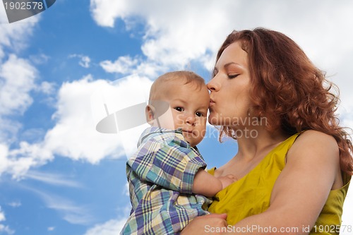 Image of mother kissing her baby on cloudy background