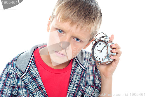 Image of Confused young kid holding time piece close to his ear