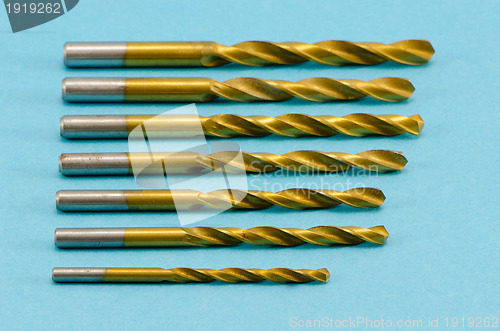 Image of various size golden drill bits on blue 