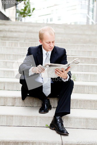 Image of young business man is reading newspaper outdoor