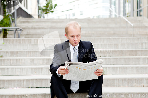 Image of young business man is reading newspaper outdoor