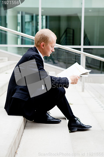 Image of young business man is reading newspaper outdoor