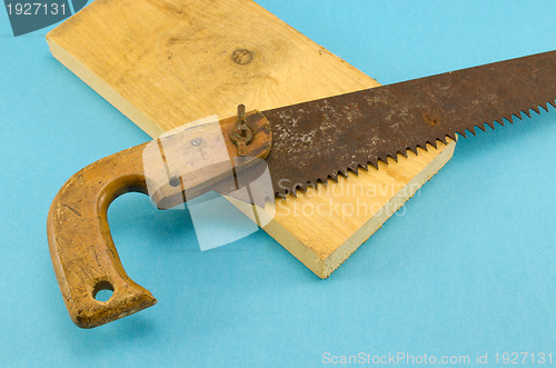 Image of retro rusty hand saw and wood board part on blue 
