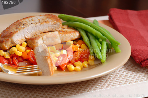 Image of Plate of pork chops resting on a bed of corn, peppers and onions