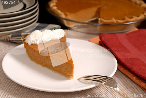 Image of Slice of pumpkin pie with extra plates resting in background alo