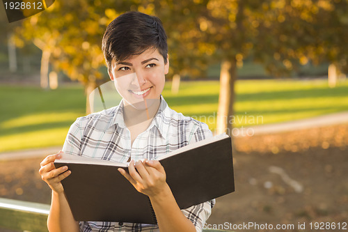 Image of Mixed Race Young Female Holding Open Book and Pencil Outdoors