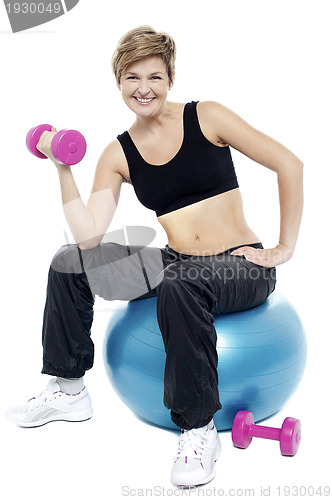 Image of Woman seated on fitness ball doing dumbbells