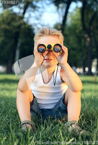 Image of Little boy sitting in the park with a binoculars