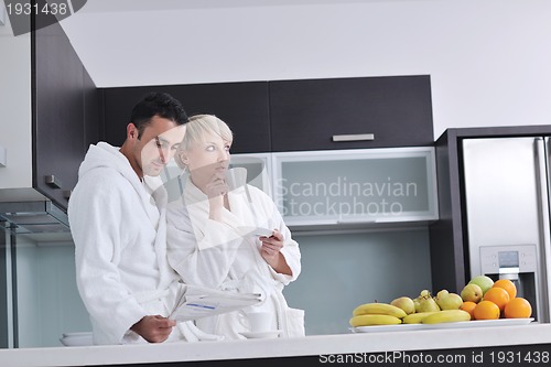 Image of Happy couple reading the newspaper in the kitchen at breakfast
