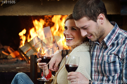 Image of Young romantic couple sitting on sofa in front of fireplace at h