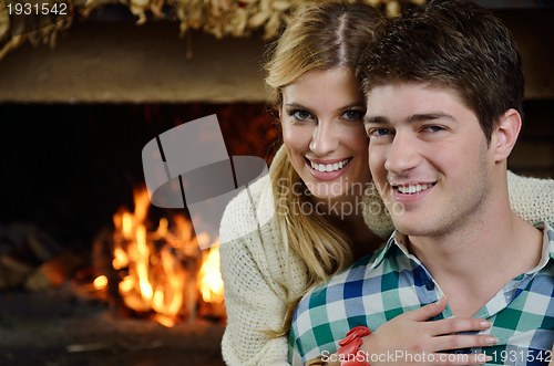 Image of Young romantic couple sitting on sofa in front of fireplace at h