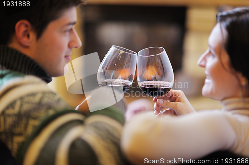 Image of Young romantic couple sitting on sofa in front of fireplace at h