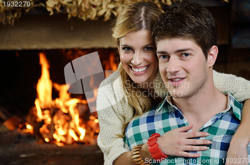 Image of Young romantic couple sitting on sofa in front of fireplace at h