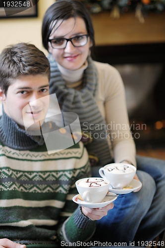 Image of Young romantic couple sitting on sofa in front of fireplace at h