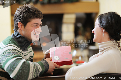 Image of Young romantic couple sitting on sofa in front of fireplace at h