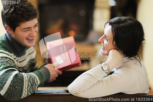 Image of Young romantic couple sitting on sofa in front of fireplace at h