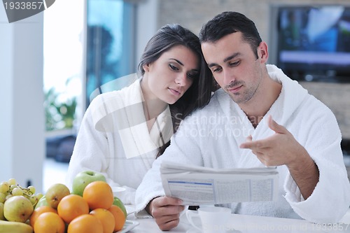 Image of Happy couple reading the newspaper in the kitchen at breakfast