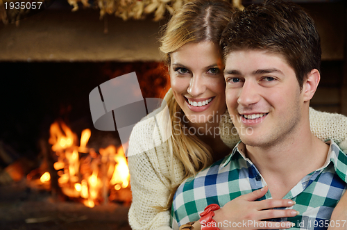 Image of Young romantic couple sitting on sofa in front of fireplace at h