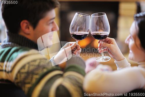 Image of Young romantic couple sitting on sofa in front of fireplace at h