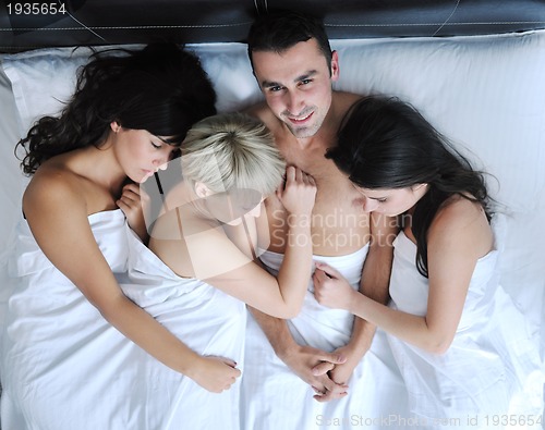 Image of Young handsome man lying in bed with three girls