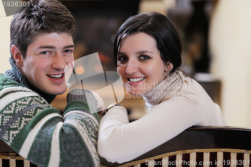 Image of Young romantic couple sitting on sofa in front of fireplace at h