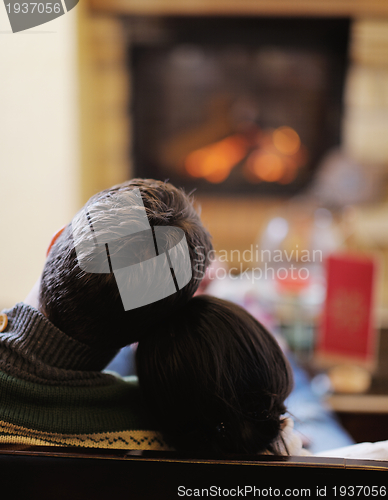 Image of Young romantic couple sitting on sofa in front of fireplace at h