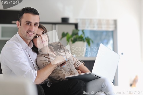 Image of joyful couple relax and work on laptop computer at modern home