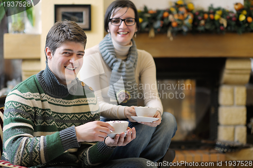 Image of Young romantic couple sitting on sofa in front of fireplace at h