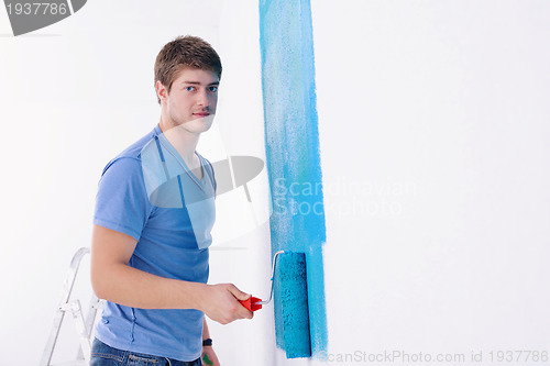 Image of handsome young man paint white wall in color