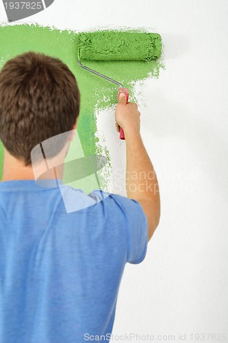 Image of handsome young man paint white wall in color