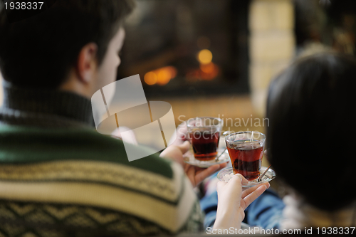 Image of Young romantic couple sitting on sofa in front of fireplace at h