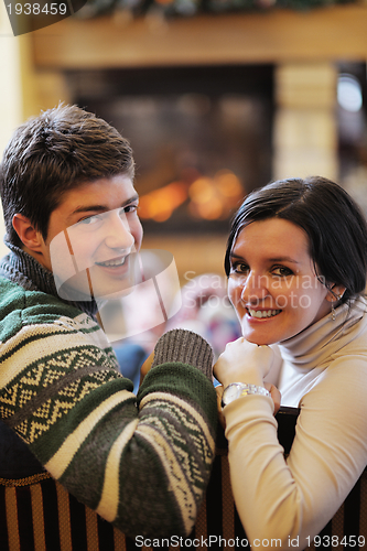 Image of Young romantic couple sitting on sofa in front of fireplace at h