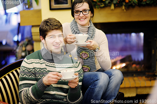 Image of Young romantic couple sitting on sofa in front of fireplace at h