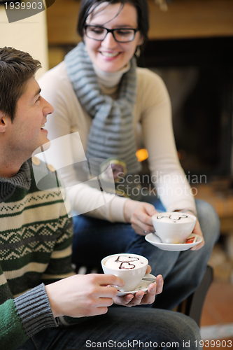 Image of Young romantic couple sitting on sofa in front of fireplace at h