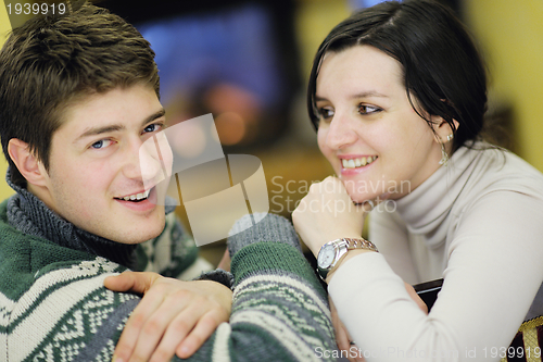 Image of Young romantic couple sitting on sofa in front of fireplace at h